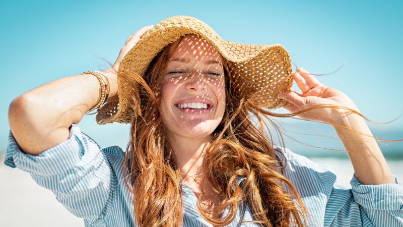 mädchen hält sich bei strahlend blauen himmel beide hände an ihrem sonnenhut