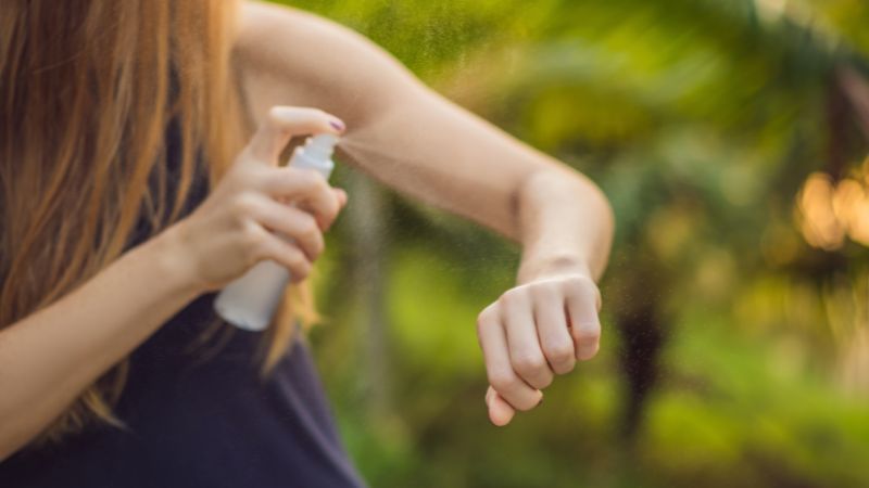 junge frau sprüht sich ein insektenschutzmittel auf den nackten oberarm