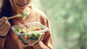 junge frau isst einen frischen bunten salat aus einer gläsernen salatschüssel