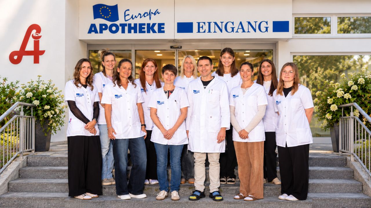 das Team der Europa Apotheke steht auf der Eingangsstiege vor dem Haupteingang der Apotheke